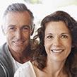 image of a couple in their 50's smiling side-by-side facing the camera