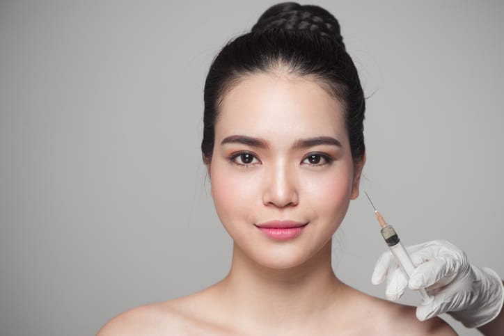 Woman smiling with syringe next to her face.