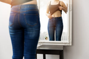 Woman looking at her new body in the mirror after having a mommy makeover