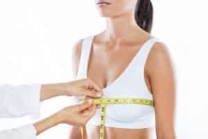 Plastic surgeon measuring a woman’s chest with a tape measure during a breast reduction consultation