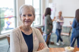 Mature woman looking happy and wearing a breast cancer pink ribbon on her shirt.